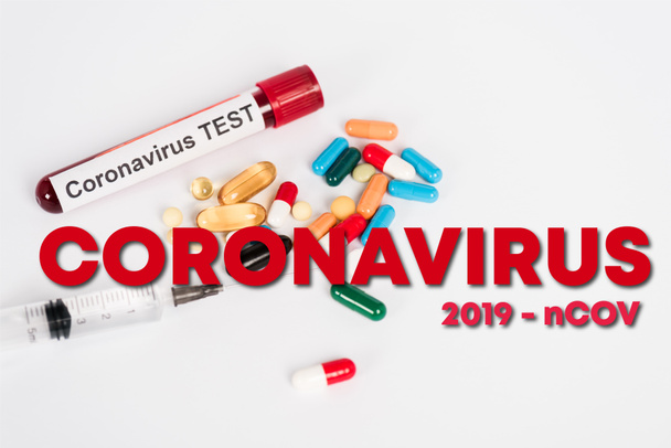 kleurrijke pillen in de buurt van monster met coronavirus test, spuit en coronavirus 2019-ncov belettering op wit  - Foto, afbeelding
