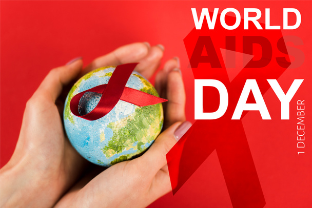 cropped view of woman holding globe with red ribbon near world aids day lettering on red  - Fotó, kép