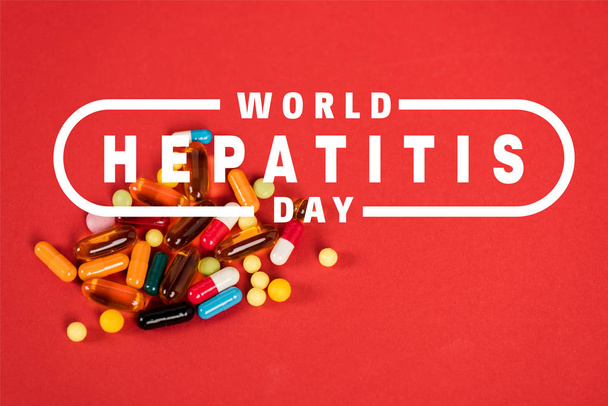 kleurrijke pillen in de buurt van wereld hepatitis dag belettering op rood  - Foto, afbeelding