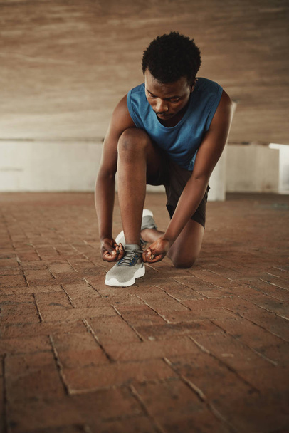 Fitness young man in sportswear tying shoelaces of sporty sneaker on pavement - Фото, зображення