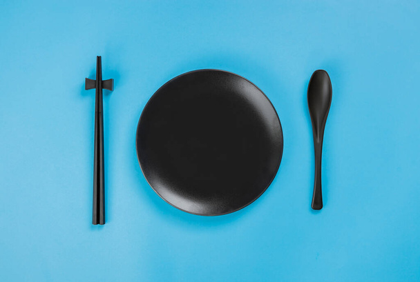 Set black plate with spoon and chopsticks on blue background - Foto, Bild