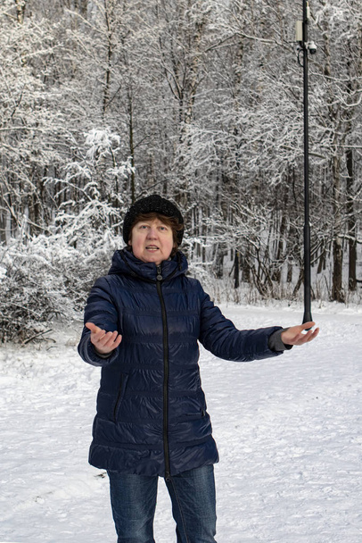 Winter. Dame mit Hut, blauer Sportjacke und Jeans vor dem Hintergrund eines verschneiten Waldes - Foto, Bild