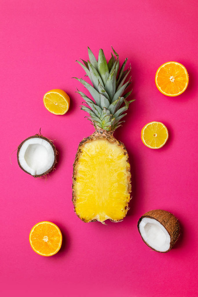 Halbe Ananas, Kokosnuss, Zitrone und Orange auf rosa Hintergrund, vertikales Foto - Foto, Bild