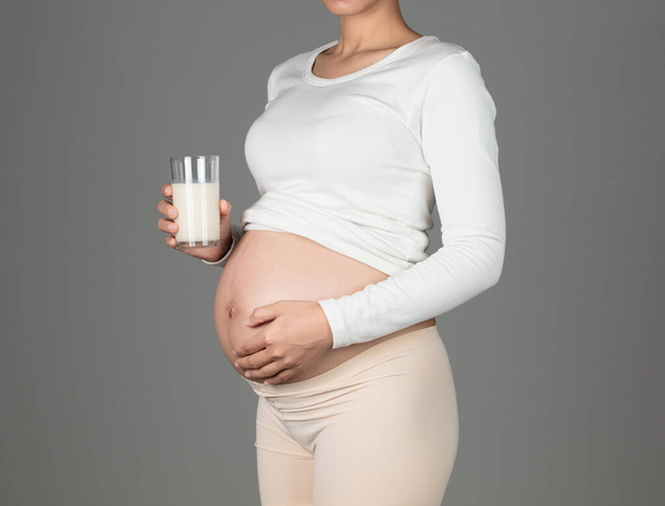 Молодая беременная женщина держит стакан молока Изолированный на серой ба
 - Фото, изображение