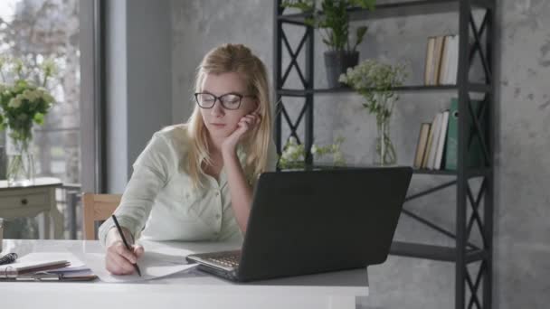 happy calm woman holds hands behind head feeling relieved relaxes and sits at home office with beautiful fresh flowers interior desk with laptop, female student enjoys successfully completed work - Imágenes, Vídeo