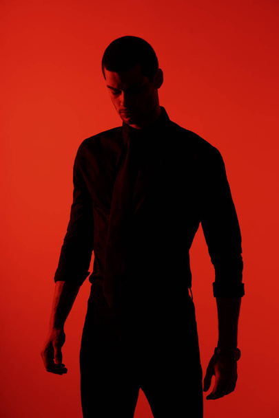 Σιλουέτα ενός νεαρού όμορφου επιχειρηματία με αυτοπεποίθηση που φοράει μαύρο πουκάμισο σε κόκκινο φως - Φωτογραφία, εικόνα