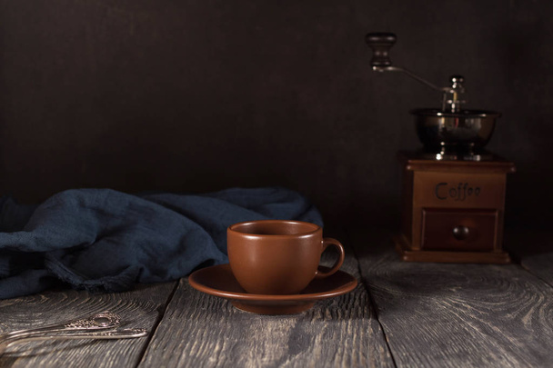 Κεραμικό Κύπελλο και πιατάκι, κουταλάκια του γλυκού, μύλος χειρός για καφέ, σε μαύρο φόντο - Φωτογραφία, εικόνα