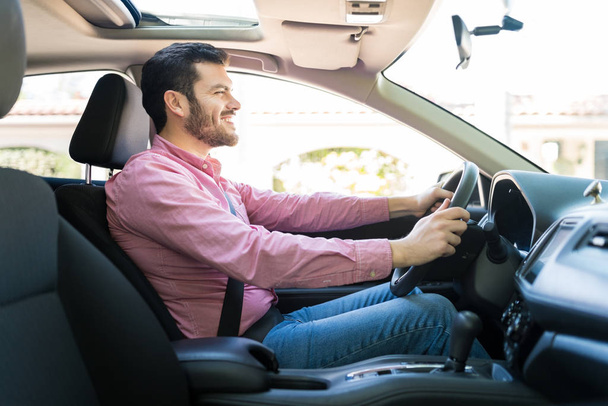 Vista lateral del hombre adulto medio latino sonriendo mientras conduce un coche nuevo
 - Foto, Imagen
