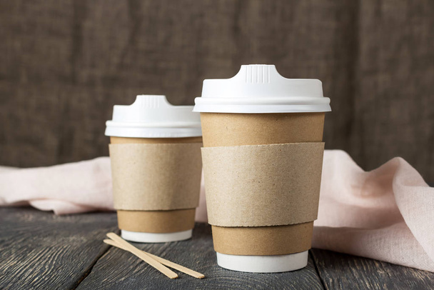 Две одноразовые чашки с кофе и деревянные мешалки рядом с легкой тканью на столе
 - Фото, изображение