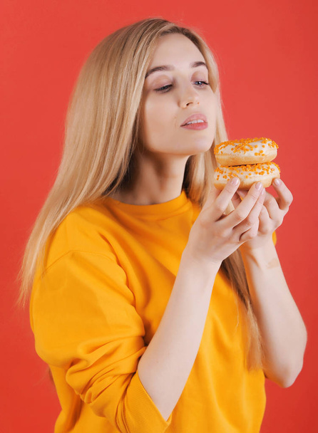 Smiling caucasian woman in yellow sweater with yellow donuts posing on red background. - Fotó, kép