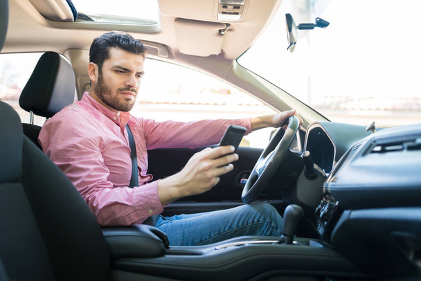 Средний взрослый красивый мужчина с помощью мобильного телефона во время вождения автомобиля в солнечный день
 - Фото, изображение
