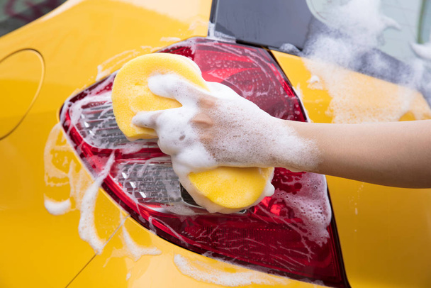 Крупный план руки с губкой Стирающий желтый автомобиль
 - Фото, изображение