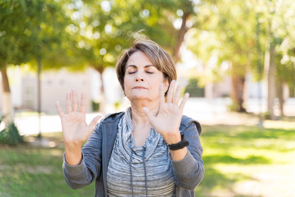 Mujer blanca mayor practicando tai chi con los ojos cerrados mientras está de pie en el parque
 - Foto, Imagen