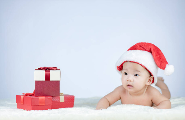 Małe dziecko leżące w kapeluszu Mikołaja w pobliżu stosu pudełek z prezentami - Zdjęcie, obraz