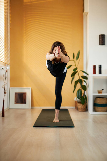 Middelbare leeftijd brunette staande in Warrior III yoga pose. - Foto, afbeelding