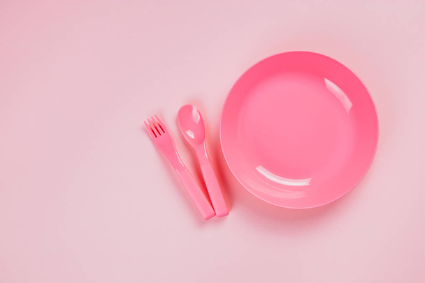 Piastra in plastica rosa con cucchiaio e forchetta su sfondo rosa
 - Foto, immagini