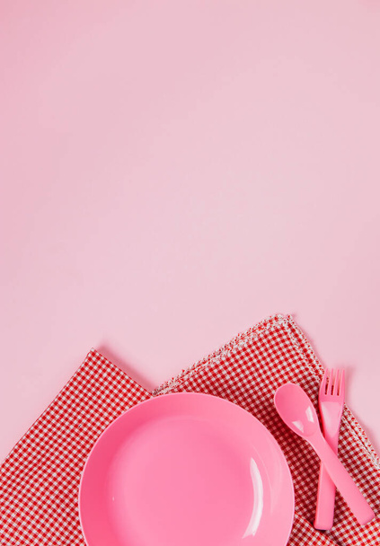 Pinkfarbener Kunststoffteller mit Plastiklöffel, Gabel und Stoffserviette - Foto, Bild