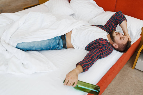 Drunken man sleeps in bed with bottle of wine. Male person with alcohol hangover, headache and depression, bad morning - Photo, Image
