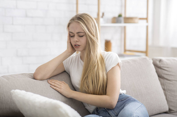 Blondes Mädchen sitzt auf Sofa und leidet an Migräne - Foto, Bild