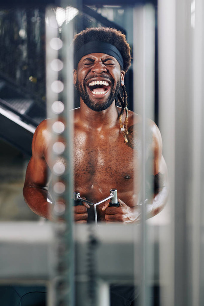 Portrait vertical de l'homme afro-américain riant de quelque chose tout en faisant de l'exercice en utilisant un appareil de fitness dans la salle de gym
 - Photo, image