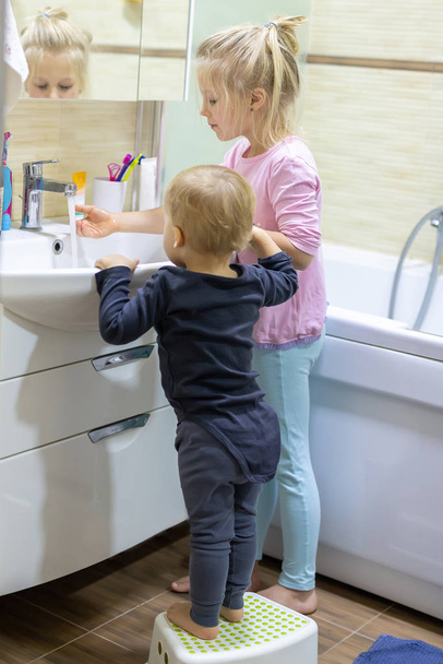 Two cute adorable blond caucasian siblings washing face and cleaning tooth with toothbrush at bathroom at home in morning. Little children brother and sister do daily higyene health care. Funny kids - Photo, Image