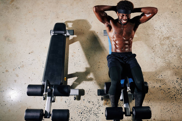Horizontal top view shot of shirtless African American man exercising on abdominal bench - Photo, Image