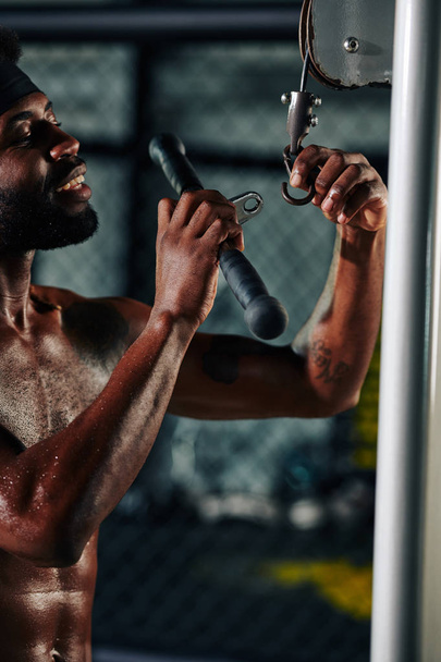 African American man standing topless changing fitness machine bar vertical shot - Photo, Image