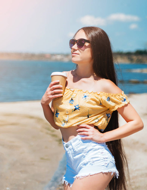 Женщина с длинными волосами пьет кофе на пляже
. - Фото, изображение