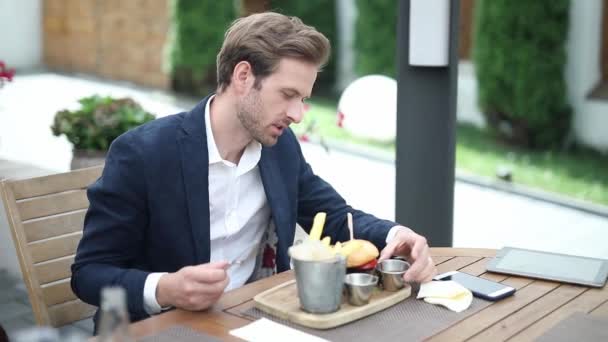 νεαρός άνδρας τρώει ένα burger με πιρούνι και μαχαίρι σε ένα εστιατόριο μπιστρό - Πλάνα, βίντεο
