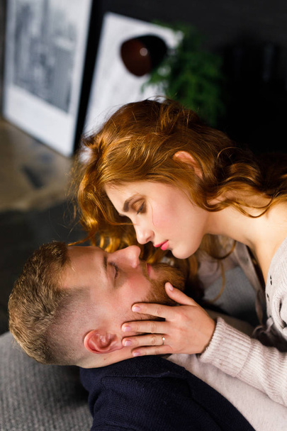 young beautiful couple having fun on a bed in a dark apartment, a girl with red hair in a white sweater and blue shorts, a man in a black sweater and white t-shirt - Φωτογραφία, εικόνα
