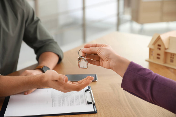 Real estate agent giving key with trinket to client in office, c - Fotó, kép