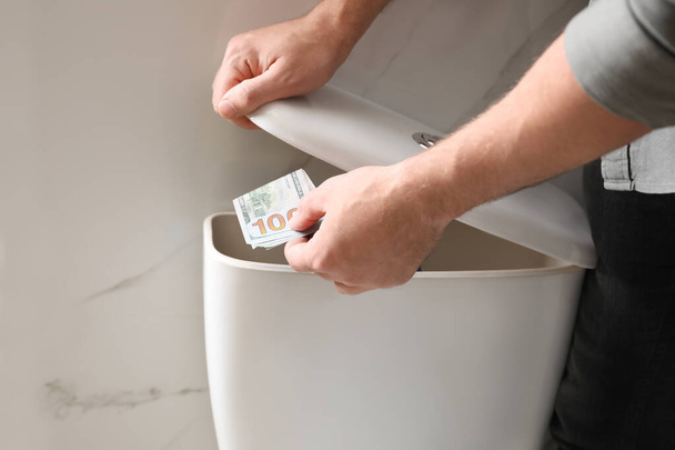 Man hiding money in toilet tank indoors, closeup. Financial savi - Fotoğraf, Görsel