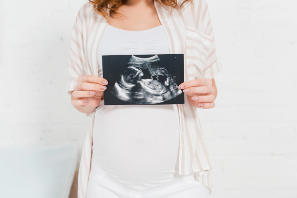 Vista recortada de la niña embarazada que muestra la ecografía del bebé en el dormitorio
 - Foto, imagen