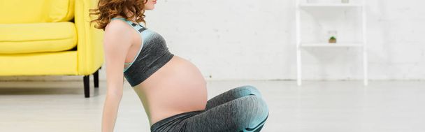 Vista recortada de la mujer embarazada en ropa deportiva sentado en el suelo en la sala de estar, plano panorámico
 - Foto, imagen