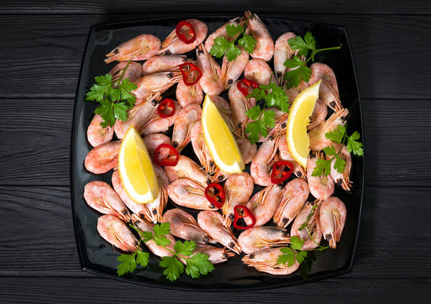 shrimp with pepper, lemon and greens on a black plate - Photo, Image