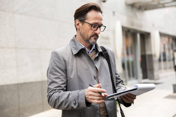 Image of serious adult businessman holding clipboard and reading - Foto, Imagem