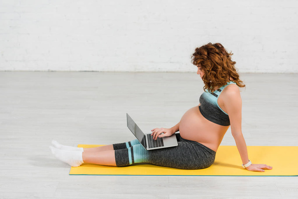 Side view of pregnant woman using laptop on fitness mat - Photo, Image