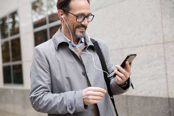 Image of joyful businessman using cellphone and earphones - Foto, Bild