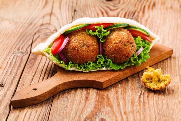 Falafel and fresh vegetables in pita bread on wooden table - Foto, afbeelding
