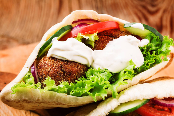 Falafel and fresh vegetables in pita bread on wooden table - Zdjęcie, obraz
