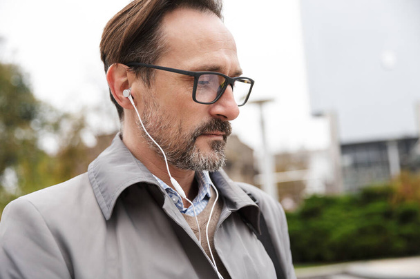 Image closeup of confident businessman using earphones while walking - Fotoğraf, Görsel