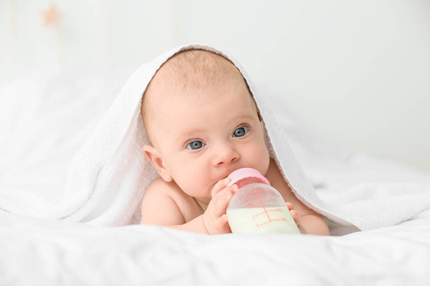 Aranyos kisbaba portréja, amint tejet iszik az ágyon lévő üvegből. - Fotó, kép