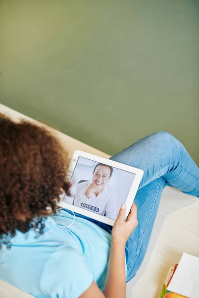 Девушка сидит на диване и разговаривает со зрелым мужчиной с помощью цифровой таблетки
 - Фото, изображение