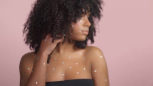 Змішана раса чорна жінка з кучерявим волоссям, покритим кришталевим макіяжем на рожевому фоні в студії
 - Кадри, відео