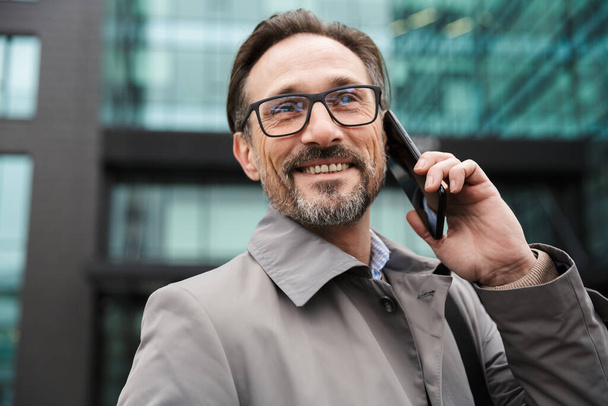 Image of smiling businessman talking on cellphone while standing - Фото, зображення
