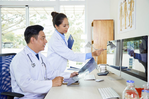 Οριζόντια λήψη δύο Ασιατών ιατρών που συνεργάζονται σε νέα ιατρική περίπτωση στο γραφείο - Φωτογραφία, εικόνα