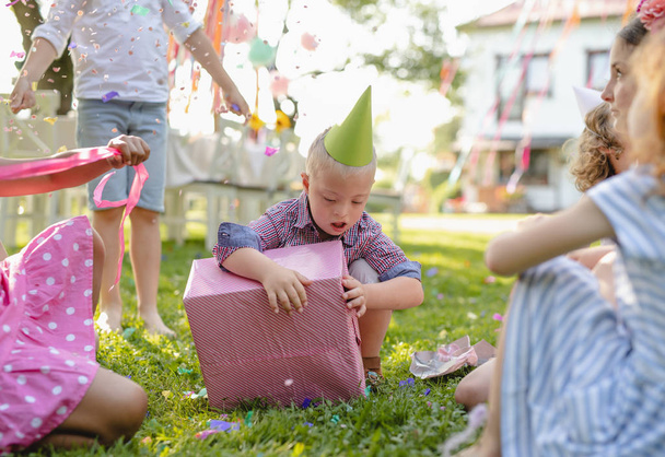 Down syndrome child with friends on birthday party outdoors, opening presents. - Zdjęcie, obraz