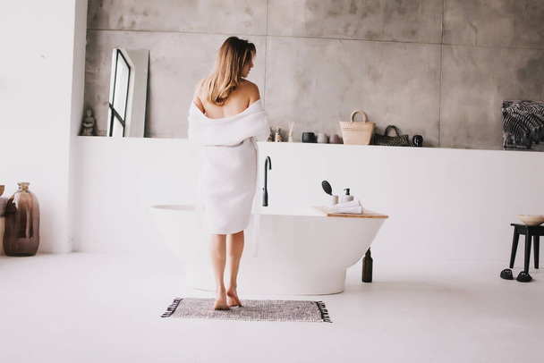Beautiful woman relaxing in white bathrobe near bath - Фото, зображення