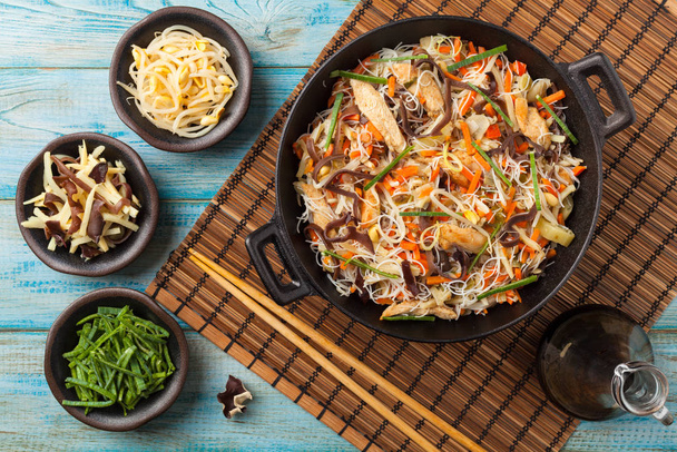 Rice noodles with chicken, mushrooms mun and vegetables in wook. - Foto, afbeelding