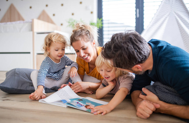 Young family with two small children indoors in bedroom reading a book. - Foto, Bild